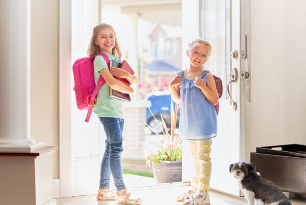 Two girls walking out of house with backpacks